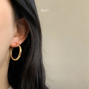 Close-up of 3cm thick gold hoop earrings worn by a model in a minimalist style
