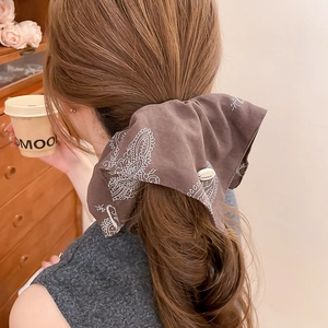 Detail of a brown paisley hair scrunchie with button on a model's ponytail