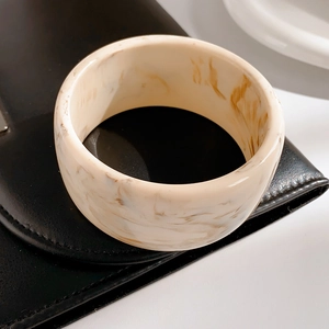 Close-up of a wide marble-patterned resin bangle with cream and brown textures