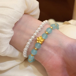 Detalle de pulsera de cuentas de piedra natural con flor dorada y perlas.