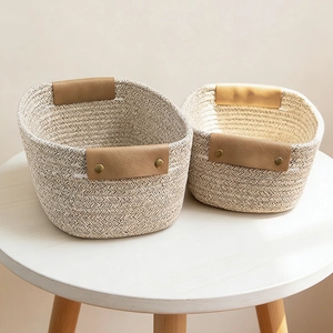 Detail of woven cotton storage baskets with leather handles and metal rivets on a white table
