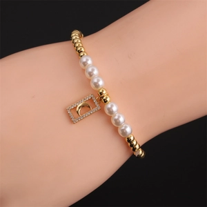 Bracciale con ciondolo a luna placcato oro e perle bianche indossato su sfondo nero intenso