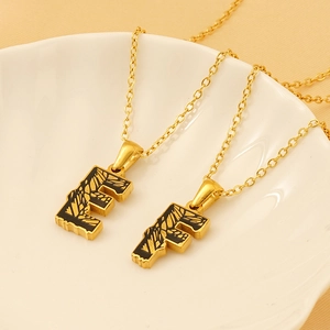 18k gold plated stainless steel letter E and F pendant necklaces on a white ceramic dish