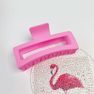 Detail view of pink matte 13cm shark hair claw clip on a flamingo coaster background