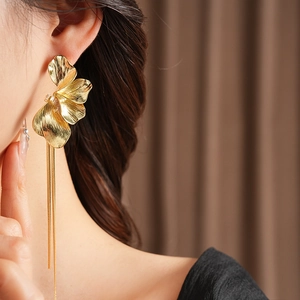 Detailaufnahme goldener Blumen-Ohrringe mit langen Quastenketten am Modell