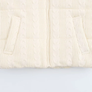 Detail of cable knit vest showing metal zipper, pockets, and textured cream white fabric