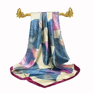 Detailed view of the square silk scarf with blue leaf patterns and purple rolled edges