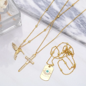 Vue détaillée des colliers en perles dorées avec pendentifs colibri, croix et œil