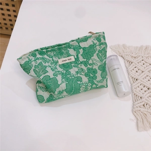 Detailed shot of green floral jacquard makeup bag with a top zipper and a fabric label