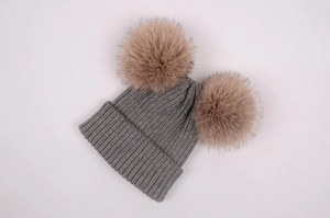 Détail d'un bonnet en tricot gris avec deux pompons en fausse fourrure marron sur fond blanc