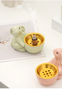 Detail of light green ceramic bunny incense burner with smoke from backflow incense cone