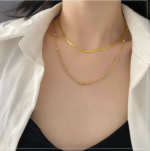 Double-layered gold snake chain and beaded necklace worn on a white shirt