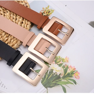 Detailed view of three colored leather belts with polished gold square buckles on a textured mat