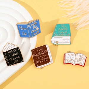 Flat lay of five colorful enamel book brooches with creative English quotes on a tray