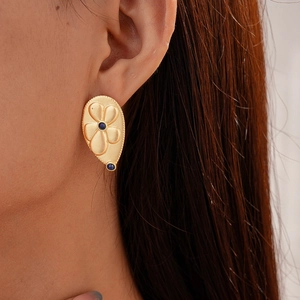 Close-up of gold flower stud earring with blue gemstone detail on model's ear