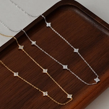 Detailed macro shot of gold and silver clover necklaces with zircon pendants on wood tray