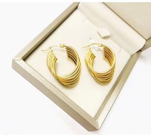 Close-up of twisted water wave 18K gold earrings presented in a beige gift box