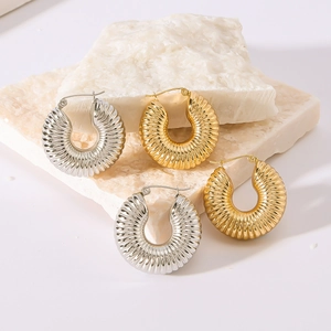 Twisted hollow hoop earrings in gold and silver finish on stone background