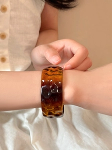 Close-up of amber resin bangle with irregular texture on a neutral fabric background
