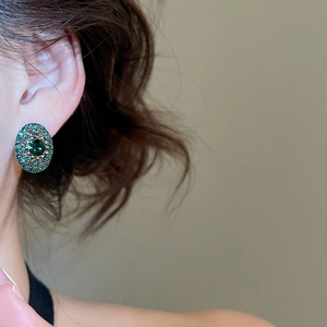Close-up of vintage oval earring with faceted emerald green gemstone and pavé rhinestones
