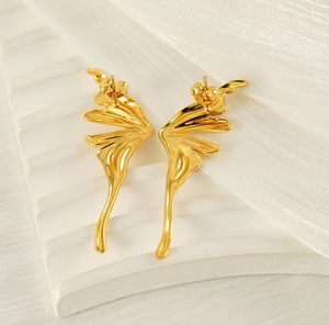 Macro shot of gold angel wing earrings with fluid metallic texture on white silk fabric