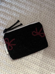 Close-up of black woven coin purse with red bow embroidery and white zipper detail