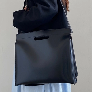 Minimalist black leather tote bag with top handles and adjustable shoulder strap for office