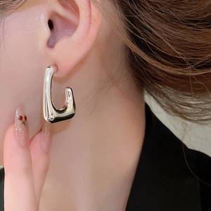 Close-up of geometric U-shaped silver metal earrings worn on ear with polished finish