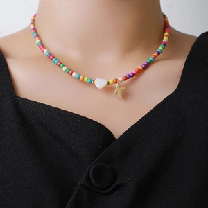 Détail du collier avec perles arc-en-ciel, pendentif cœur et breloque lettre K dorée
