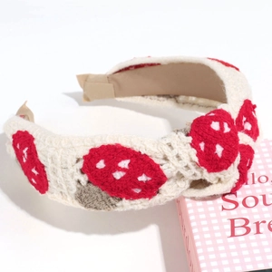 Close-up of a cream knitted headband featuring embroidered red and brown mushroom patterns