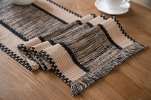 Detail of woven cotton table runner with black and beige stitching and fringe tassels