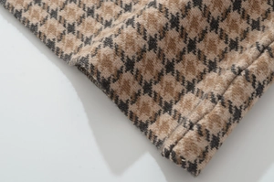 Detailaufnahme von braunem Hahnentritt-Wollstoff mit Webstruktur und Saumnähten am Saum