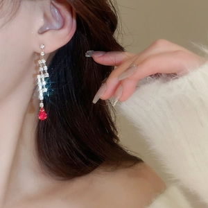 Close-up of long gold earrings with square gems and red teardrop pendant on model