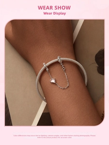 Detalle de pulsera de malla de plata s925 con dije de corazón y cadena de seguridad en la muñeca