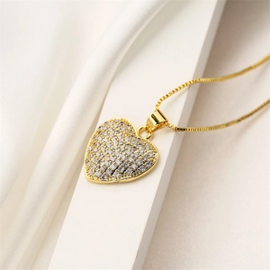 Macro shot of gold heart pendant with cubic zirconia inlay on elegant white silk fabric