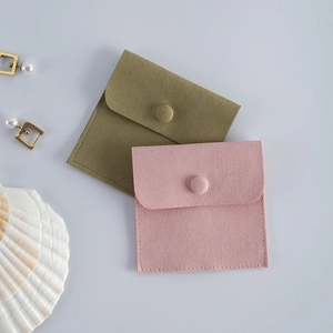 Pink and moss green velvet jewelry pouches with snap buttons on a minimal grey background