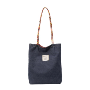 Sac cabas en jean bleu avec anses tissées et écusson blanc sur fond blanc