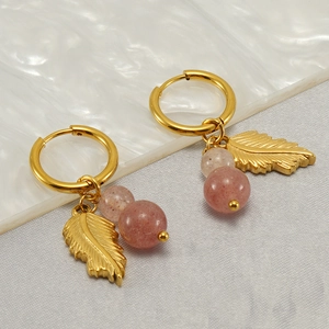 Detail of gold leaf drop earrings with pink turquoise stones on marble background