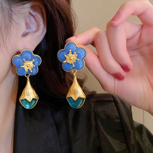 Detailed shot of retro blue flower earrings with gold accents and emerald green pendants