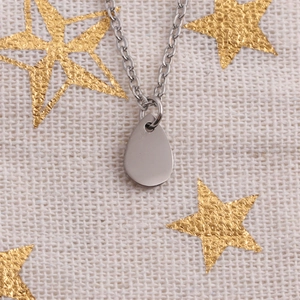 Vue détaillée du collier pendentif en forme de larme argentée sur tissu en lin à étoiles