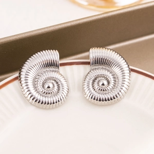 Macro shot of silver conch shell earrings on a white ceramic plate with brown trim