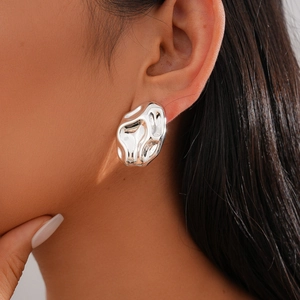 Close-up of model wearing silver earrings with irregular lava fold texture and glossy finish
