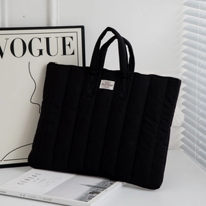 Close-up of black quilted laptop sleeve with vertical stitching and woven brand label