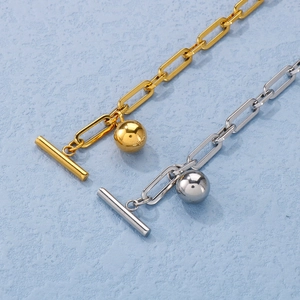 Detailed close-up of gold and silver paperclip chain bracelets with toggle clasp and round pendant