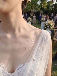 Close-up of gold and silver star tattoo stickers on collarbone with white lace dress