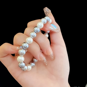 Detailed view of gray and white pearl bracelet on model's wrist with black background