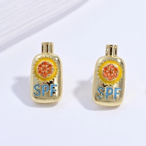 Macro shot of gold sunblock bottle stud earrings with sun gem and SPF lettering