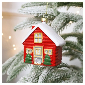 Detail of red and white house-shaped Christmas ornament hanging on a snowy tree branch