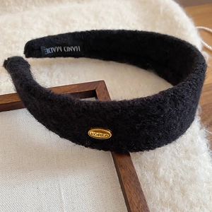 Détail du serre-tête en peluche noire avec emblème Korea doré et étiquette faite main
