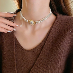Close-up of double-layer pearl necklace with a rhinestone oval pendant in golden finish